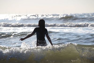 Rear view of silhouette girl standing in splashing sea
