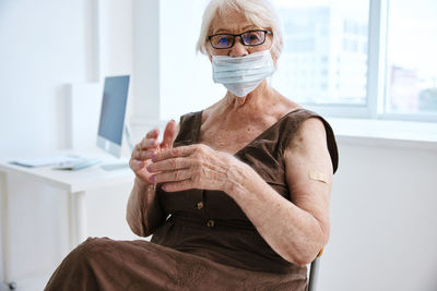 Portrait of senior woman wearing mask sitting at clinic