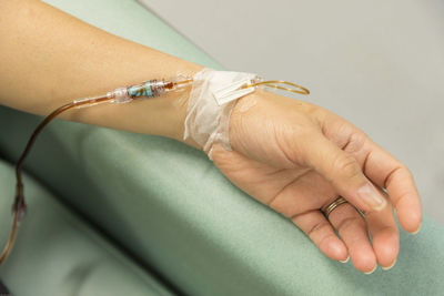 Cropped hand of woman with iv drip on bed in hospital