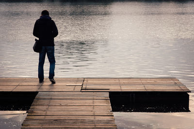 Rear view of man standing on jetty over lake during sunset