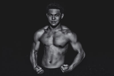 Portrait of confident bodybuilder showing build against black background