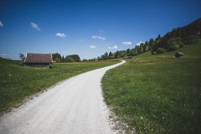 Empty road amidst field against sky