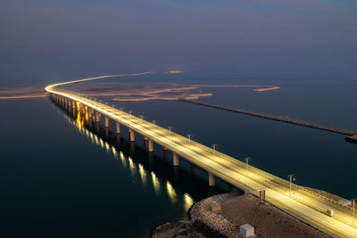 Illuminated bridge over river against sky at night