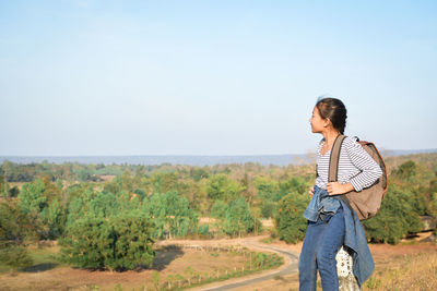 Girl with backpack looking at landscape against sky