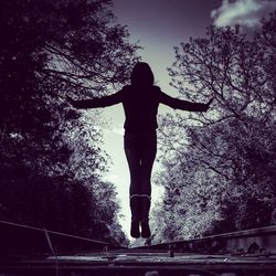 Rear view of silhouette woman standing by tree against sky