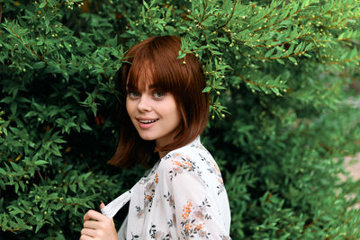 Portrait of young woman standing against plants