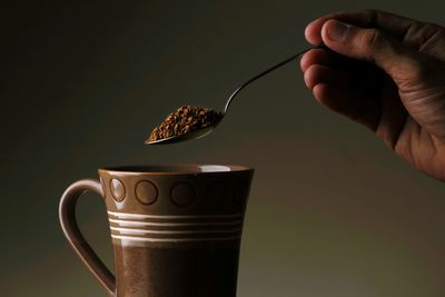 Cropped person holding spoon of ground coffee against gray background