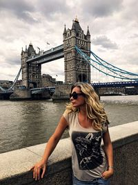 Young woman leaning on retaining wall against tower bridge