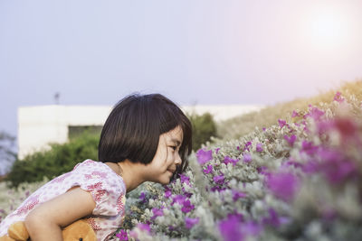 Side view of cute girl smelling flowers against sky
