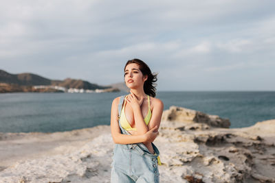 Carefree young woman standing on sand at beach against sky