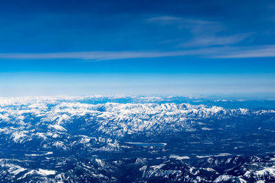 Aerial view of snowcapped mountains against blue sky