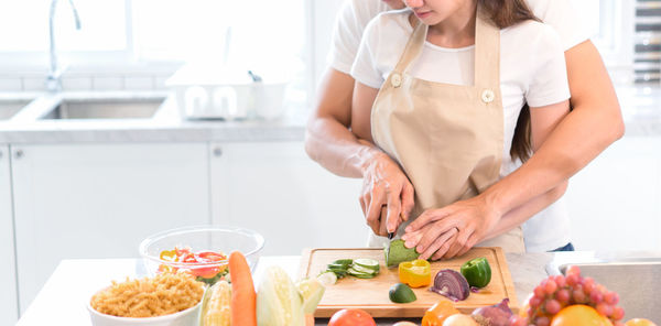 Midsection of young couple looking at each other while cutting zucchini together in kitchen