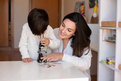 Mother assisting son in puzzle sitting at home