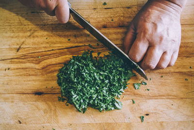 Cropped hand of person cutting cilantro on table