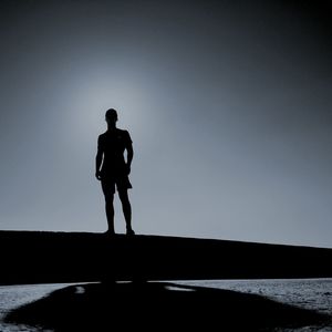 Silhouette man standing by sea against clear sky