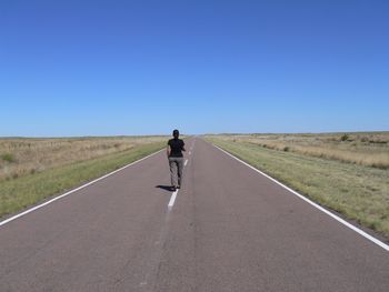 Rear view of man walking on road against sky