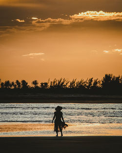 Silhouette woman walking at beach against sky during sunset