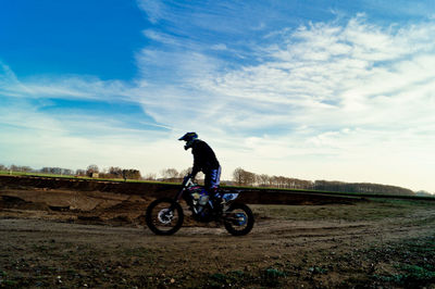 Side view of man performing stunt while riding motorcycle on dirt road against sky
