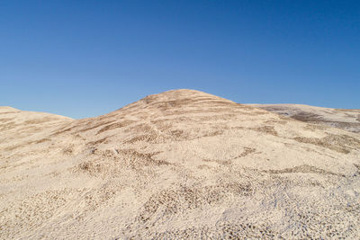 Low angle view of desert against clear blue sky