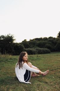 Young woman relaxing on field against clear sky