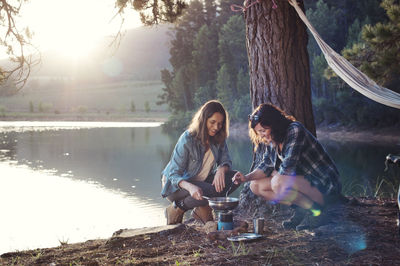 Female friends making food by lake at campsite