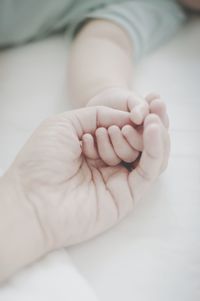 Cropped hand of mother with baby on bed