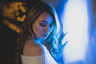 Close-up of young woman looking down in illuminated room