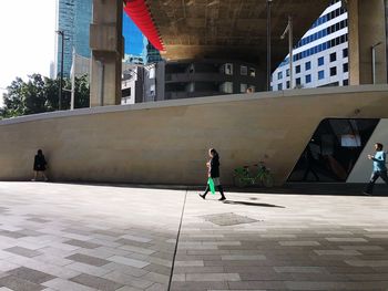 Rear view of woman walking on footpath against buildings in city