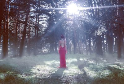 Young woman standing by tree in forest against sky