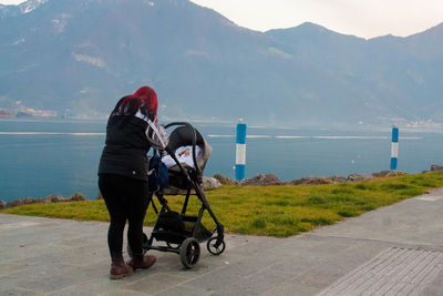 Rear view full length of woman standing with baby stroller by lake