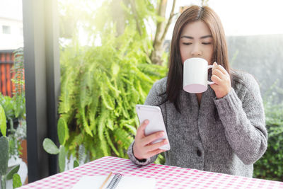 Young woman holding coffee cup on mobile phone