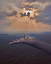 Cropped hand of woman holding ganesha against sky during sunset