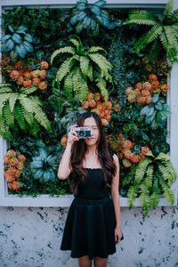 Full length portrait of young woman standing against plants