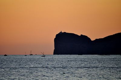 Silhouette rocks by sea against clear sky during sunset
