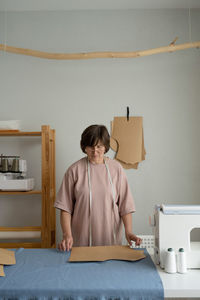 Focused professional dressmaker with measuring tape making patterns on fabric while working at table with special equipment in light atelier