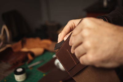 Treats edges with sandpaper. tanner makes leather wallet, professional craftsman, closeup, indoors, 