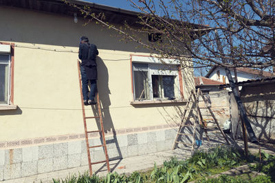 Rear view of man standing on ladder outdoors