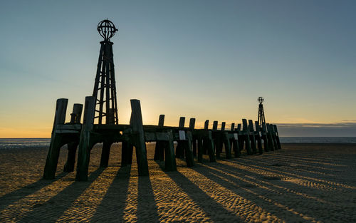 Wooden posts on beach against clear sky during sunset