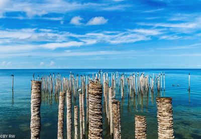 Wooden posts in sea against sky