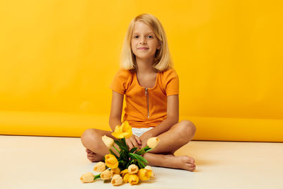 Girl with flower sitting against yellow backdrop