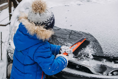 Cute little boy cleaning snow off the car at winter backyard. little kid toddler boy helping father