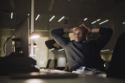 Mature businessman with hands behind head working late in office at night