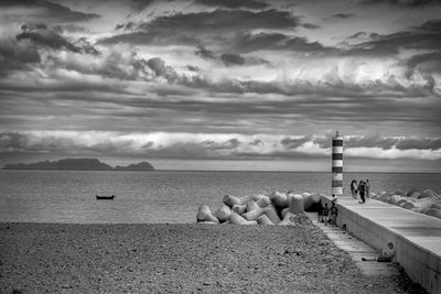 People on jetty by lighthouse overlooking sea