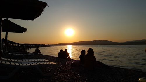 Silhouette people sitting at beach against clear sky during sunny day