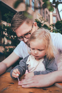 Daughter painting father's fingernails at table outdoors