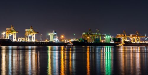 Illuminated city by sea against clear sky at night