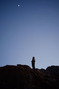 Low angle view of man standing on cliff against clear sky