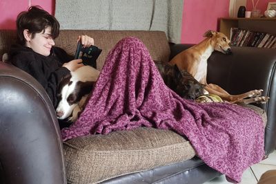 Girl using smart phone while sitting with dogs on sofa at home