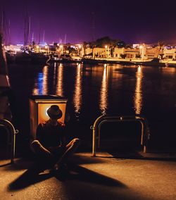 Man sitting at harbor in city during night