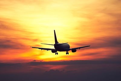 Silhouette airplane flying against dramatic sky during sunset